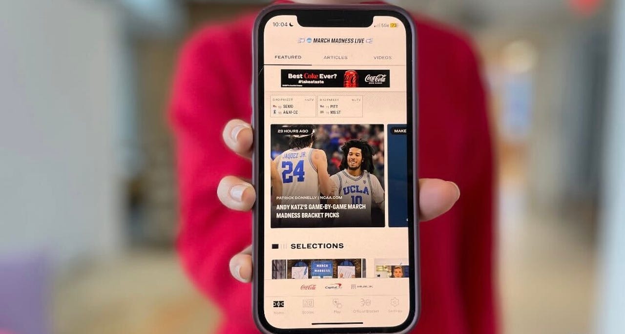 Young woman in a red sweater holding up the NCAA March Madness Live app on an iPhone.