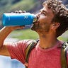 Man drinking from a water bottle while hiking outside