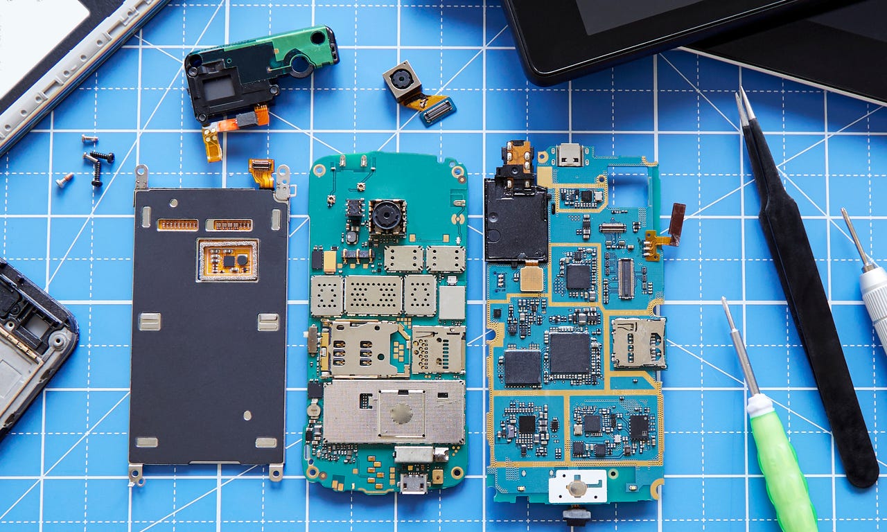 Deconstructed smartphone with tools around it on a blue background