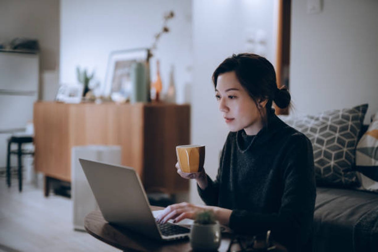 Woman using laptop while holding coffee cup