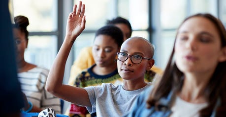 A black college student raises her hand in a classroom.