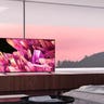 A Sony X90K on a platform in front of a window which shows a pink sunset over a pine forest
