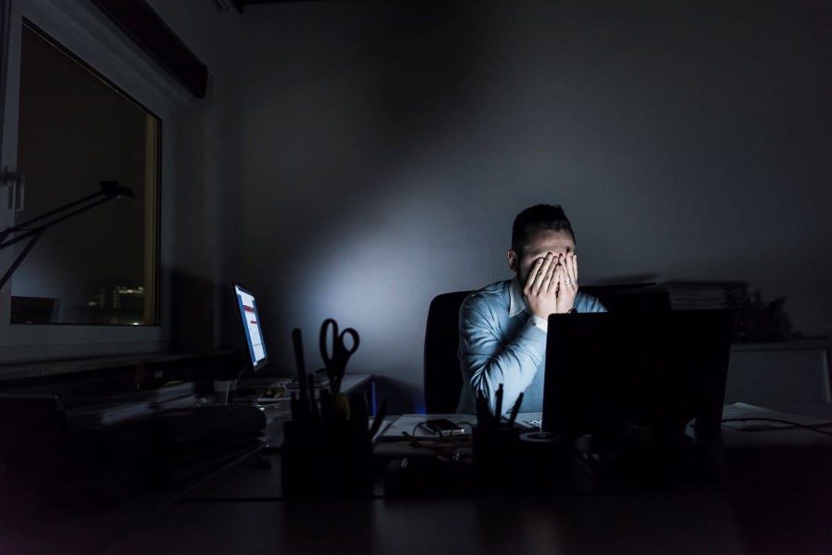 Man at computer screen in dark room, head in hands looking stressed out :(