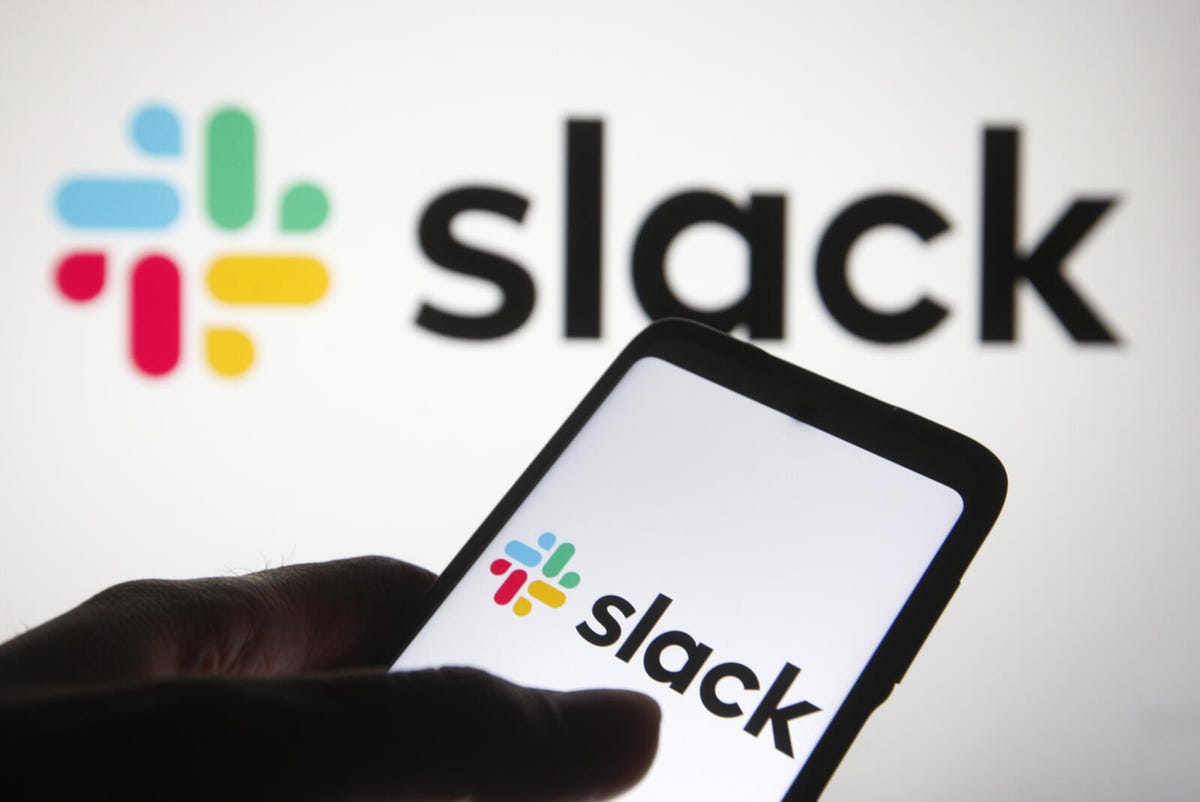 Hand holding a phone showing the Slack logo, in front of a larger Slack logo