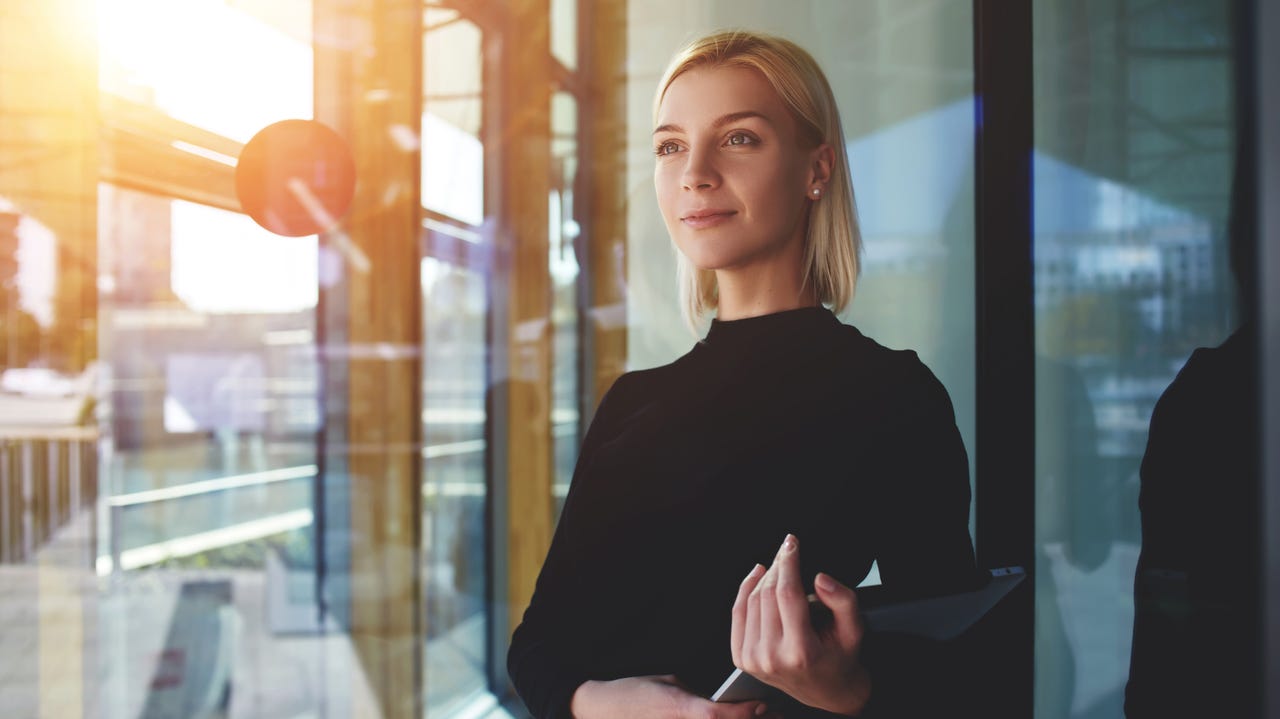 A white female executive wearing a black turtleneck smiles while gazing out a window.