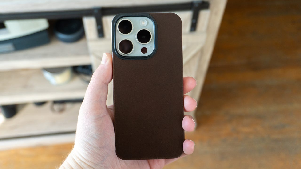 Holding the iPhone 15 Pro with the Nomad Magnetic Leather Back in Rustic Brown.
