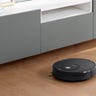 A black Roborock cleaning the floor in front of a grey dresser