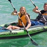 Woman and man in life vests on a green inflatable kayak and smiling while paddling