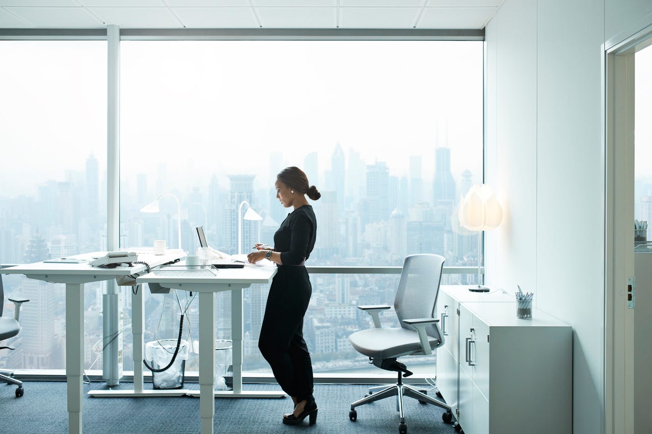 Woman working on her laptop at a standing desk with city view in background