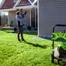 Wide shot of a man in a jacket and jeans using a Greenworks pressure washer to clean the siding of his house.