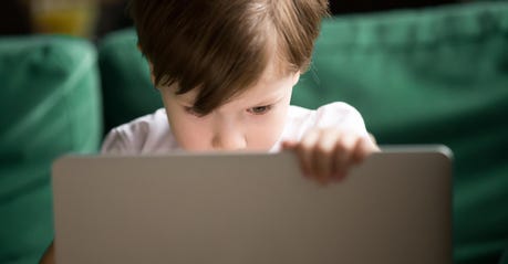 Curious kid boy secretly watching forbidden censored content on laptop