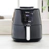 A black air fryer on a white kitchen counter next to wooden spoons
