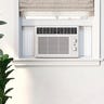 An air conditioner unit in a bedroom window next to a plant