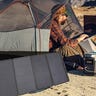 A man in a tent using an EcoFlow Delta 1000 generator and solar panel to power his laptop in the desert