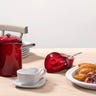 Red French press on a kitchen table with pastries and flowers
