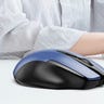 A blue and black wireless mouse on a desk with a person working on a laptop in the background