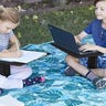 Two children sitting on a blanket on the grass with lap desks in their laps